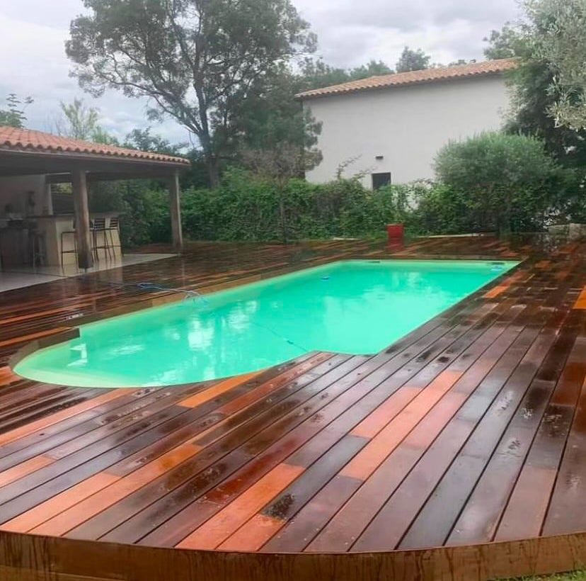 Grande terrasse en bois exotique autour d’une piscine dans un jardin arboré
