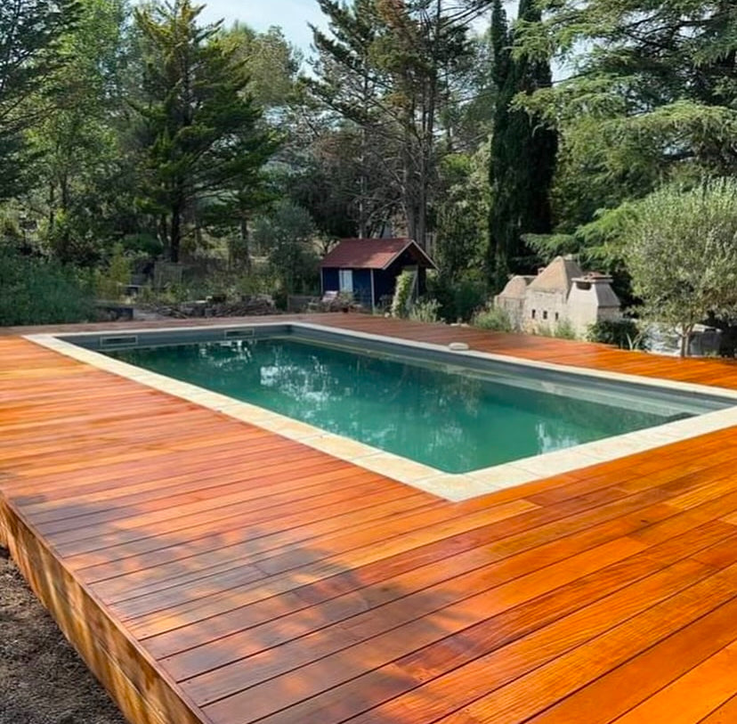 Grande terrasse en bois exotique autour d’une piscine dans un jardin arboré
